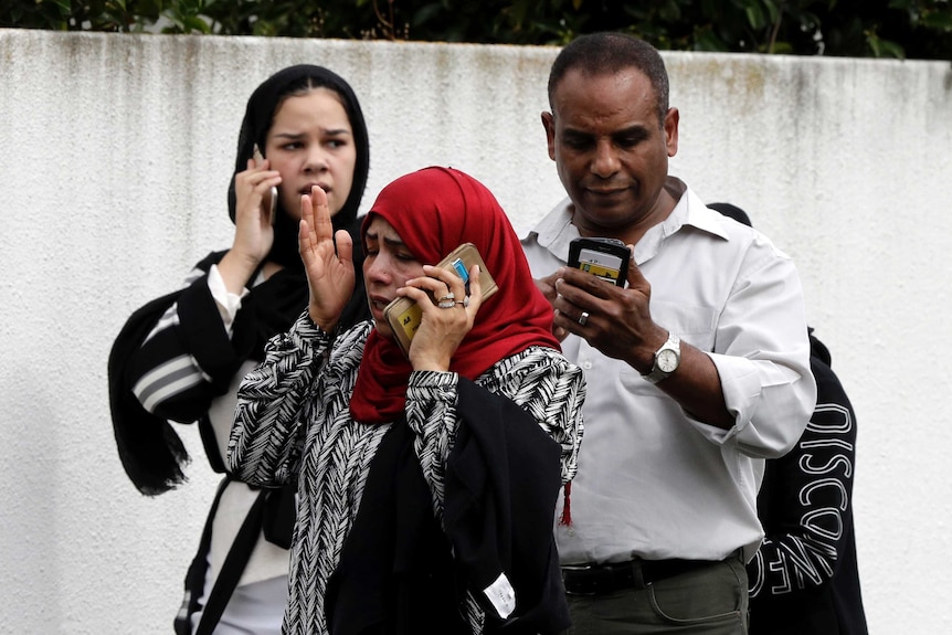 People wait outside a mosque on the phone