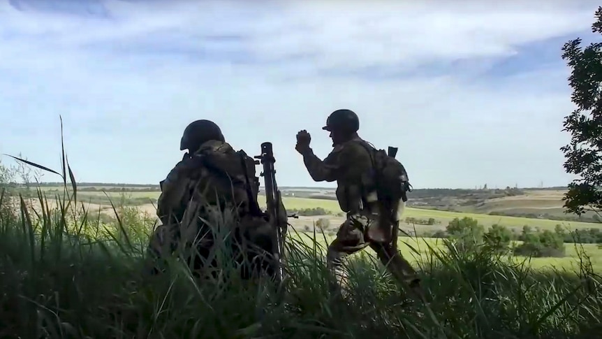 Two soldiers are seen operating a mortar in a grassy field.