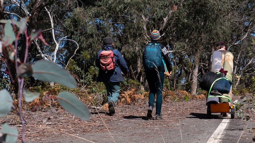 Three people walking down abandoned road with carpets on a trolley.