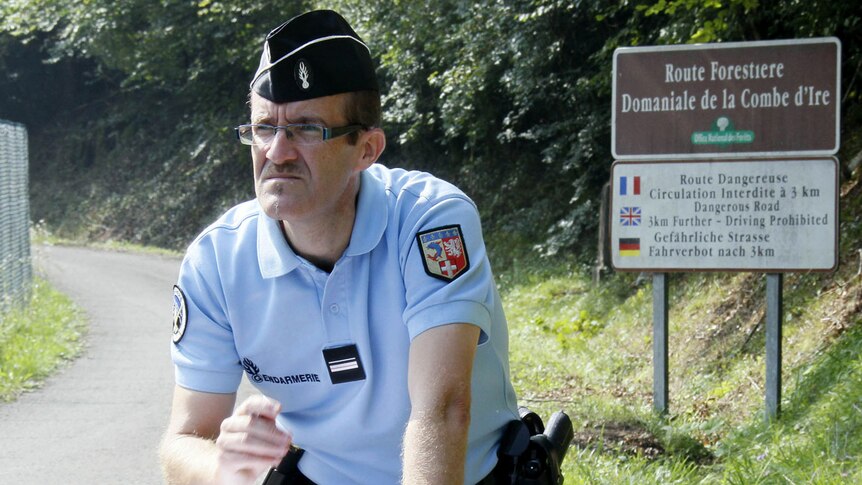 A French gendarme checks his notes as he blocks the access road to La Combe d'Ire