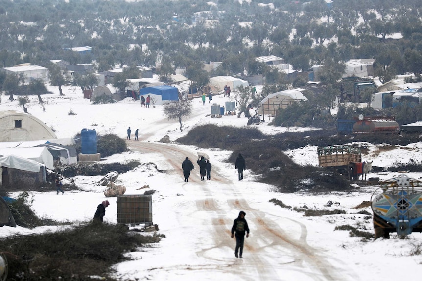 People wander through a snow-covered makeshift refugee camp.