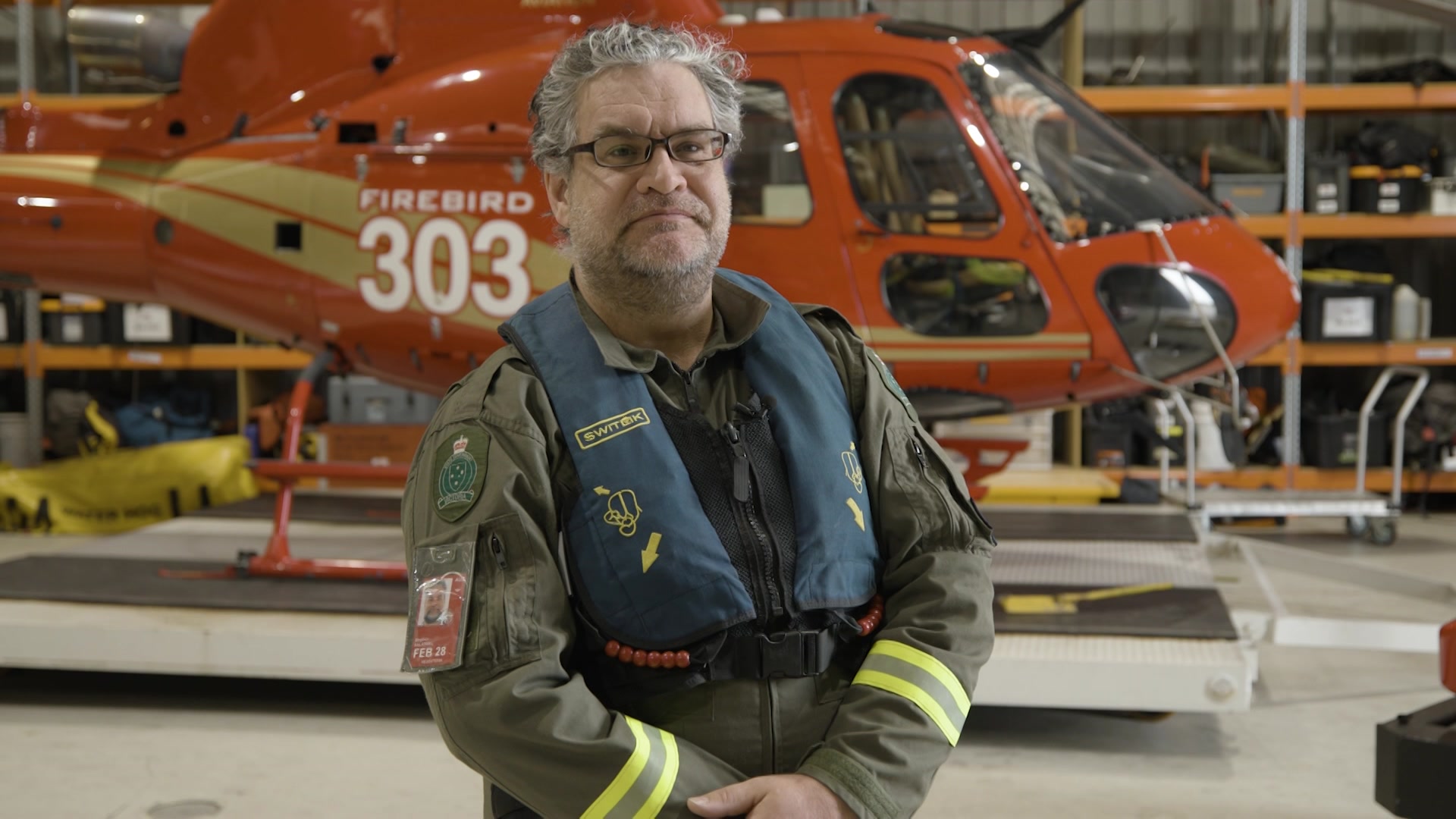 A man wearing a flight uniform stands in front of a helicopter.