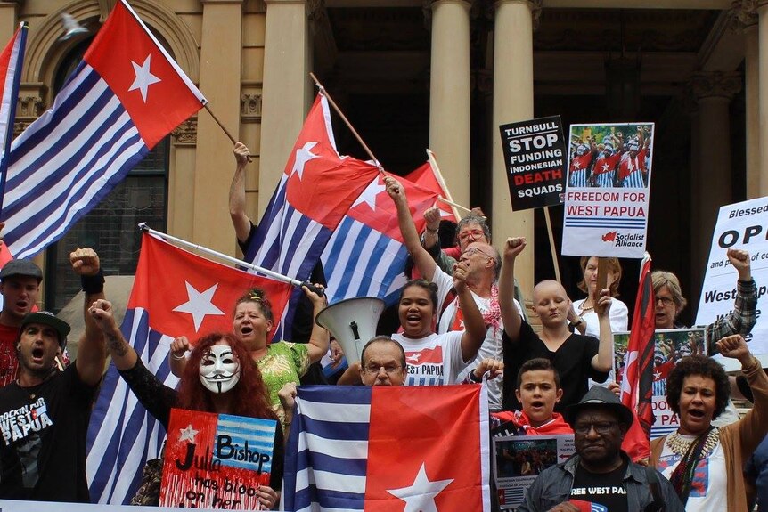 A group of people wave flags and signs that say: Freedom for West Papua".