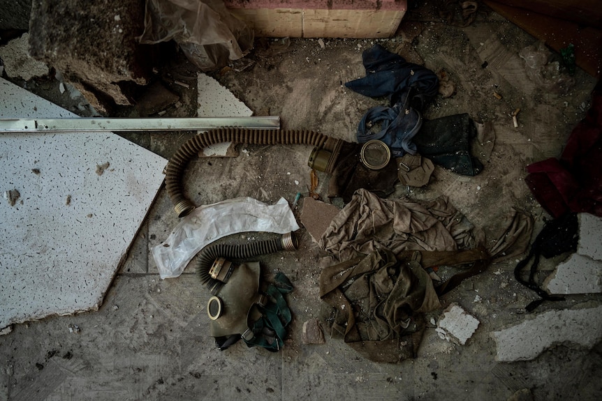 Gas masks are among the rubbish lying on a dirty floor, viewed from the top down.