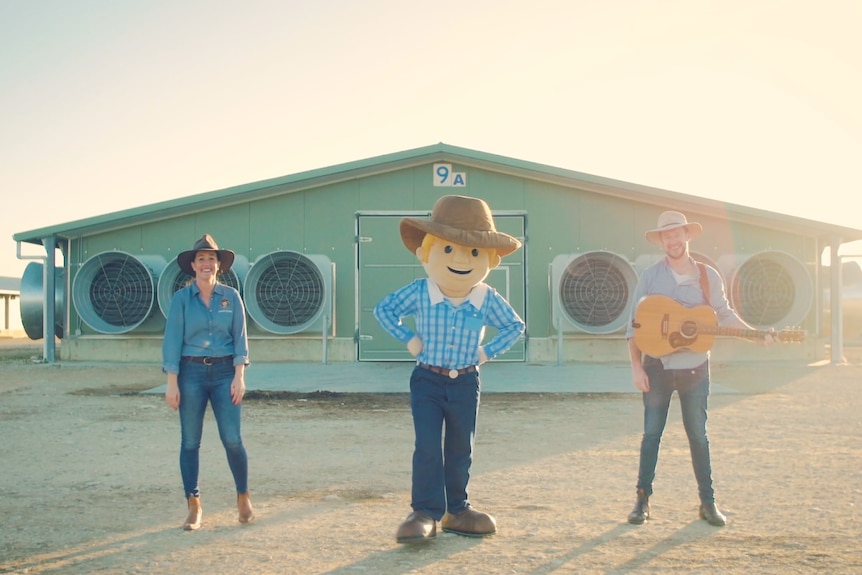 The costume character, George the Farmer, stands flanked by a woman on the left, and a man with a guitar on the right.