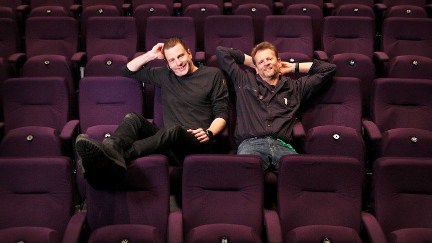 Two men leaning back in empty rows of theatre seats