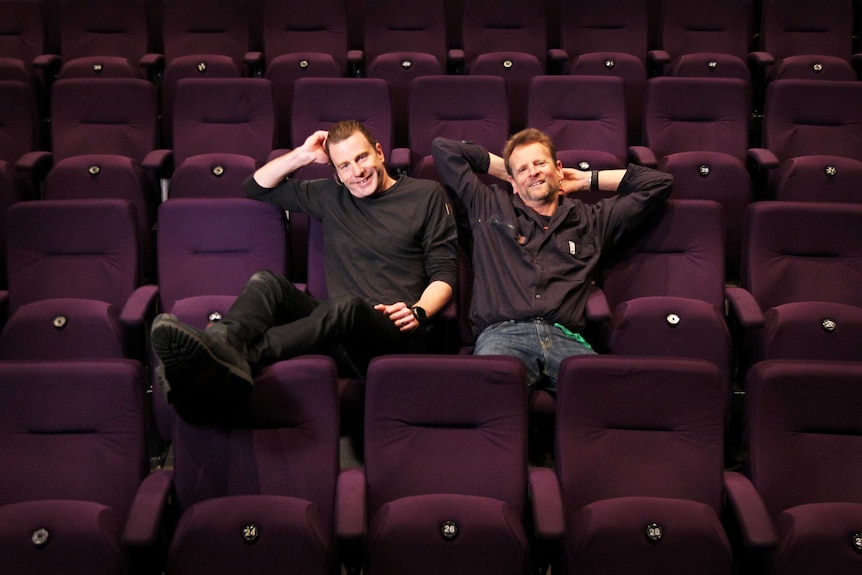 Two men leaning back in empty rows of theatre seats