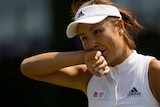 Peng shuai wearing white tennis gear and hat brings her right arm to her face on court