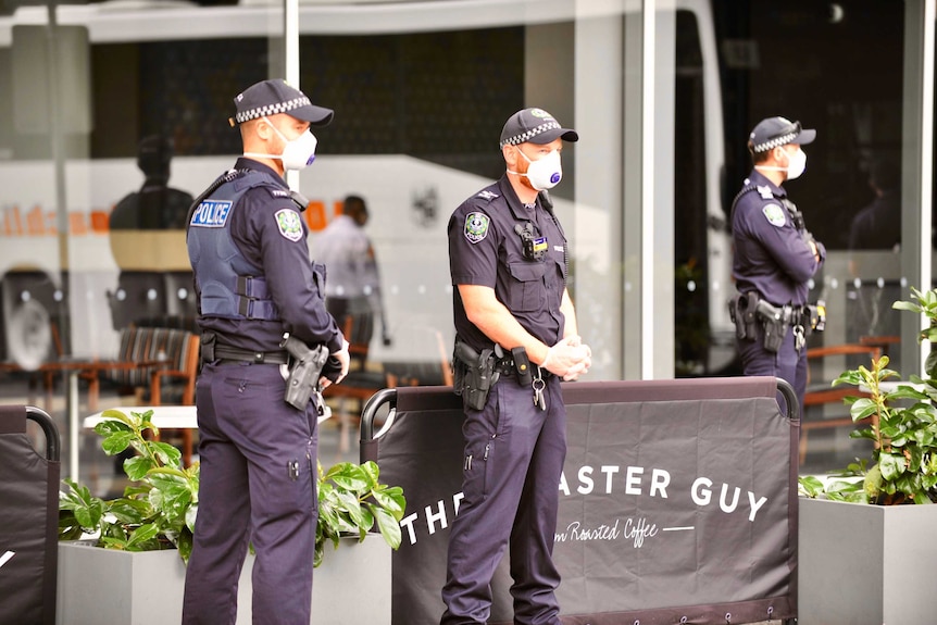 Three police officers in blue uniforms wearing white face masks