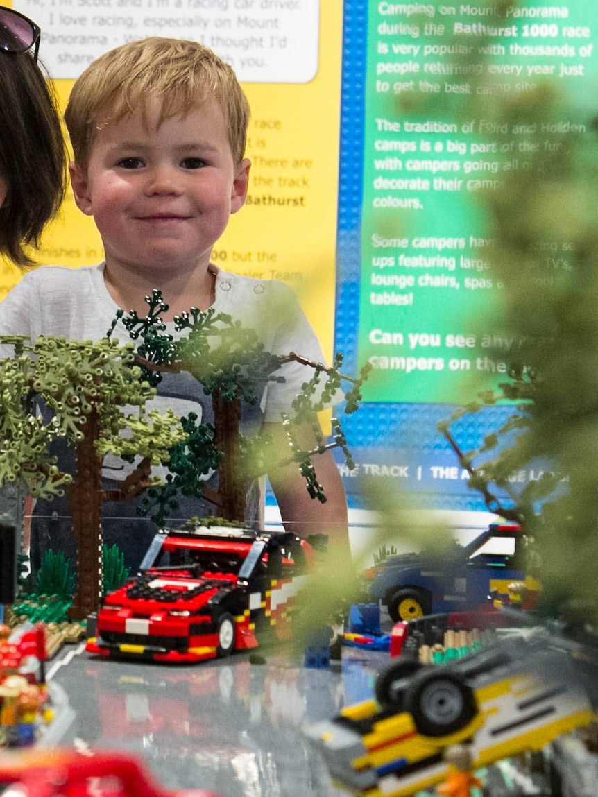 A boy looking at a lego model of cars and trees