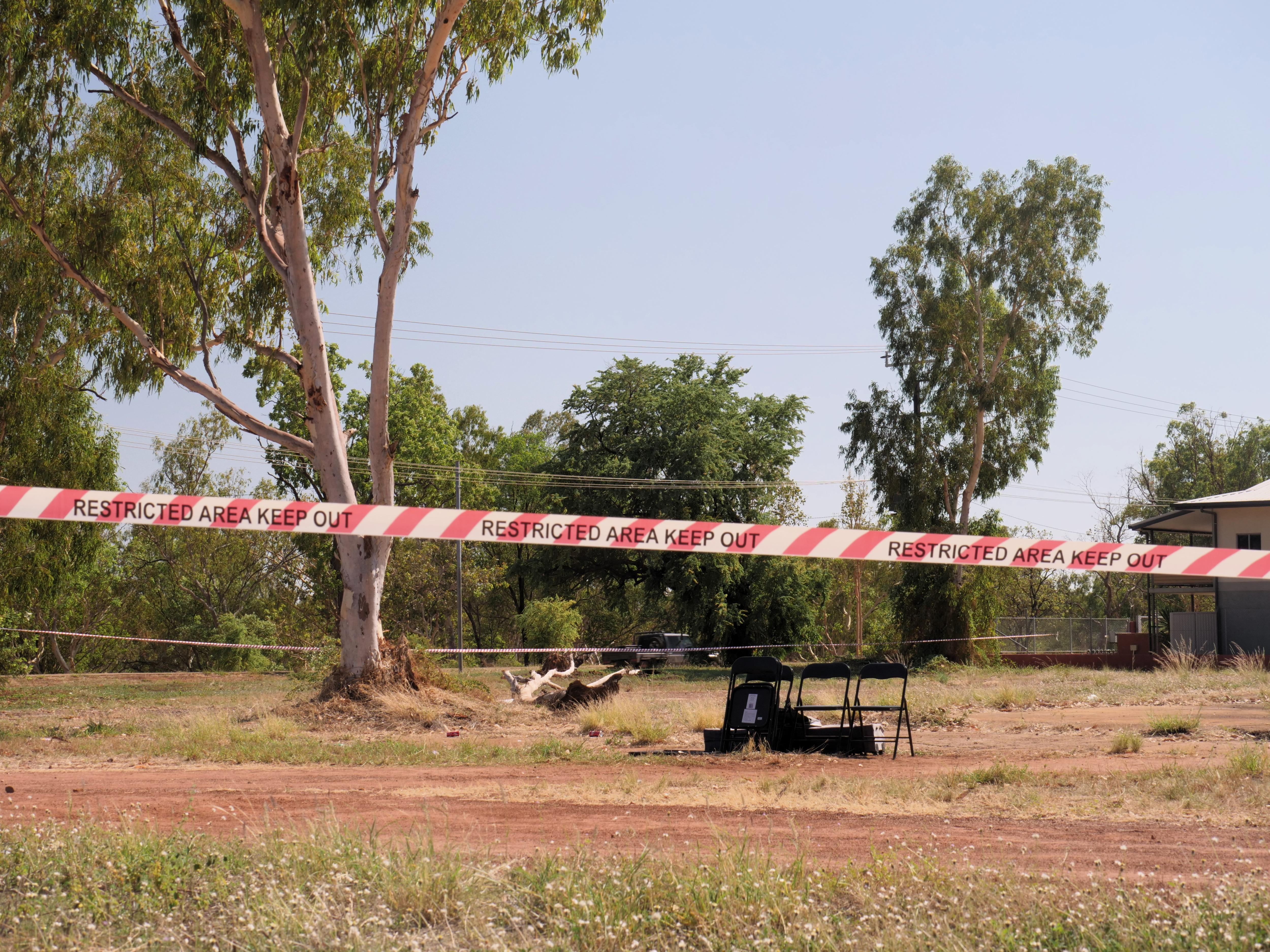 An empty block of land, taped off by police crime scene tape, with a few empty chairs in the middle.
