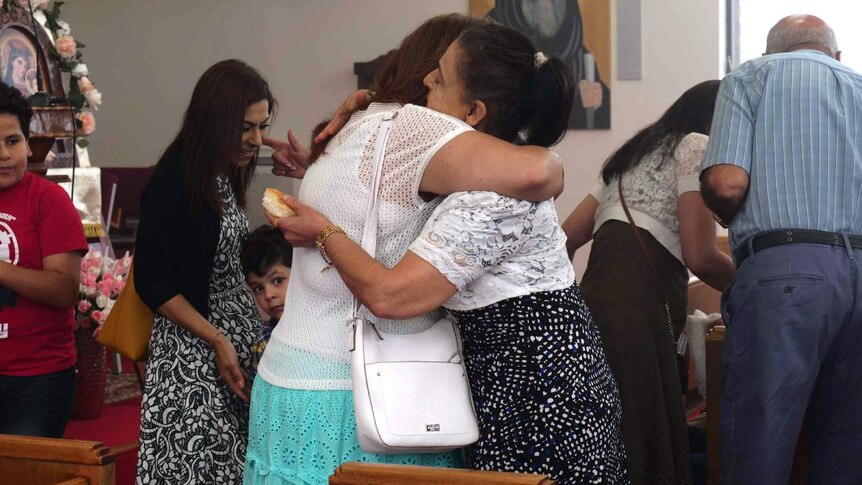 Two women hug each other inside a Coptic Orthodox Church.