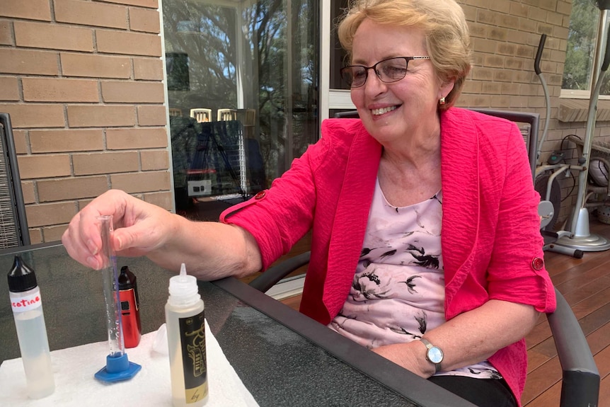 Dianne Gorman sits outside holding a tube next to small bottles of liquid.