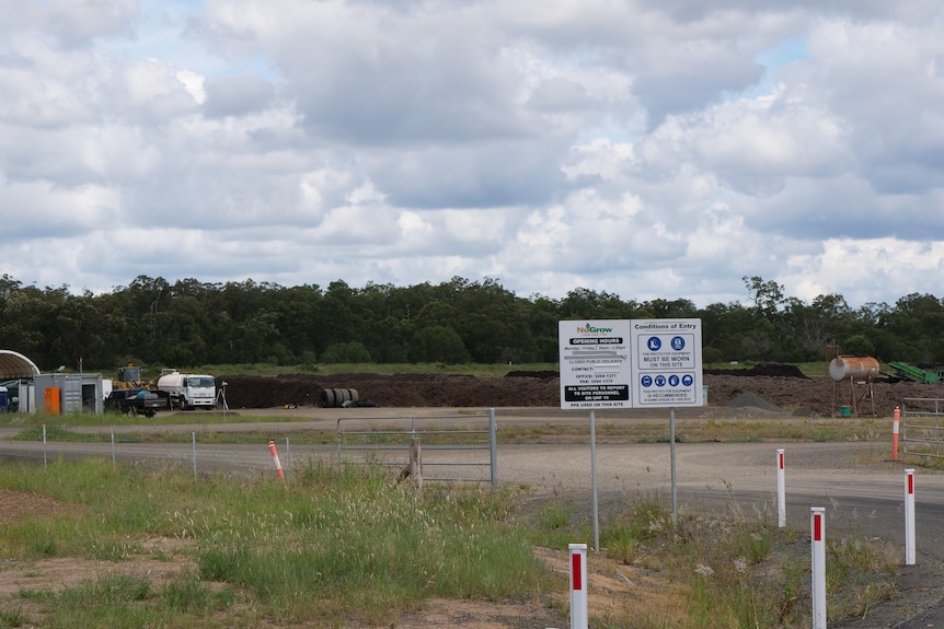 A sign reading NuGrow sits in front of the entrance to a waste plant with vehicles and soil in the background.