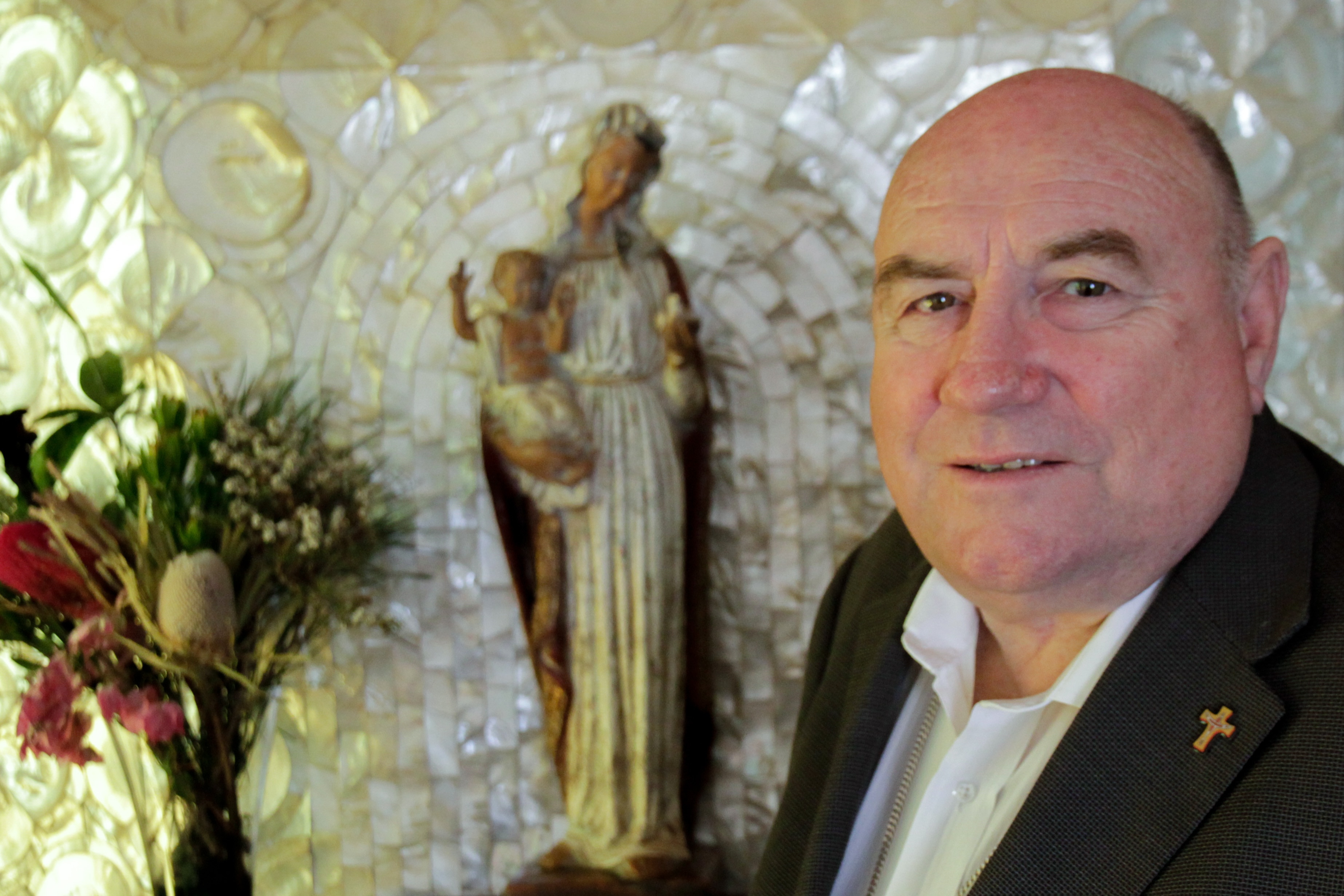 Close up of a man's face in front of a statue of Mary and Jesus 