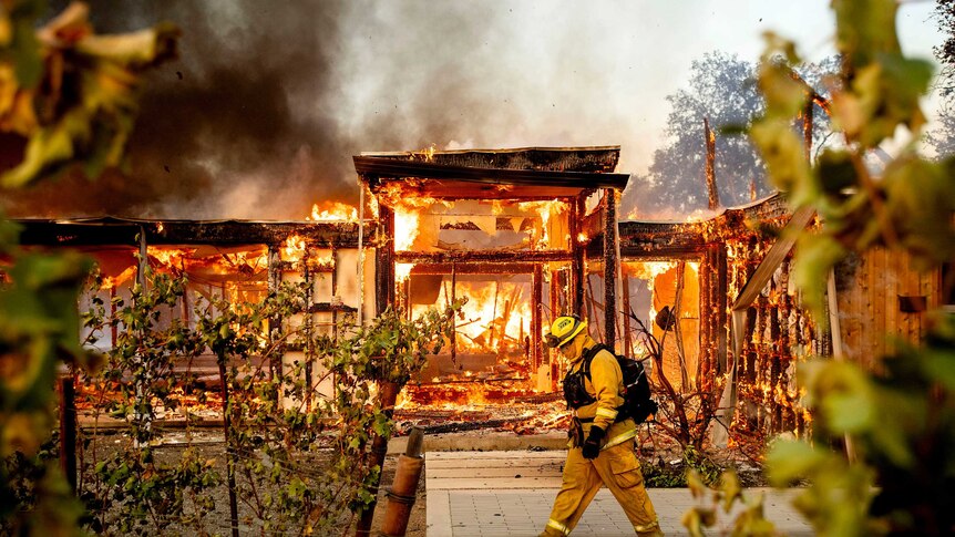 A firefighter walks past a house hollowed out by flames.