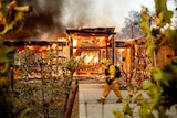 A firefighter walks past a house hollowed out by flames.