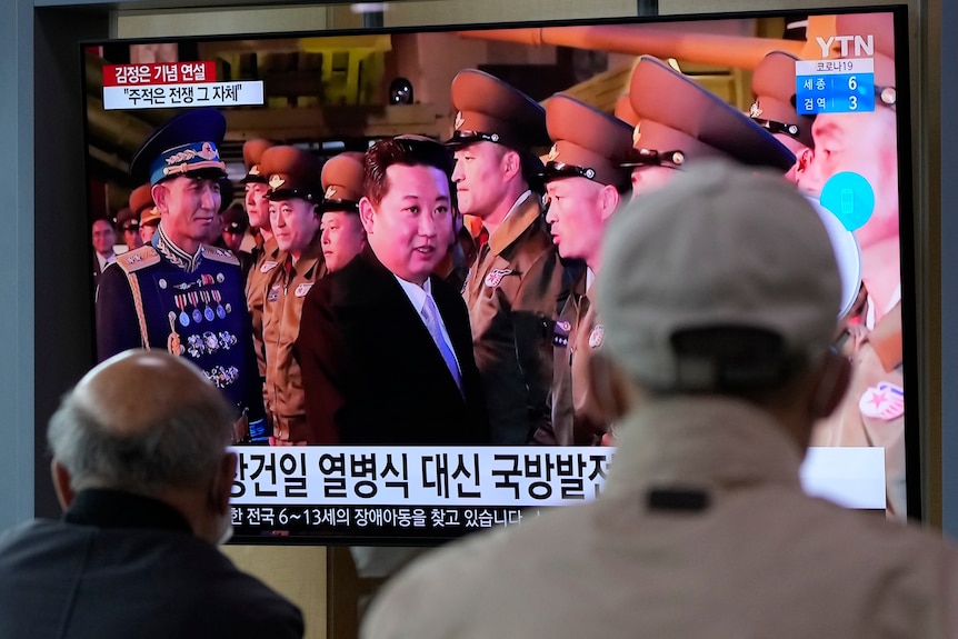 Persone in una stazione ferroviaria guardano lo schermo TV del leader nordcoreano Kim Jong Un durante una parata militare