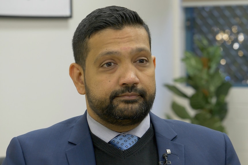 A man wearing business attire has a serious expression while being interviewed.