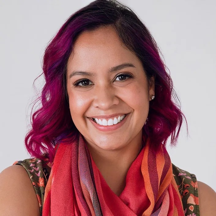 Uma foto profissional de Sahra O'Doherty, que tem cabelo magenta e usa lenço rosa.