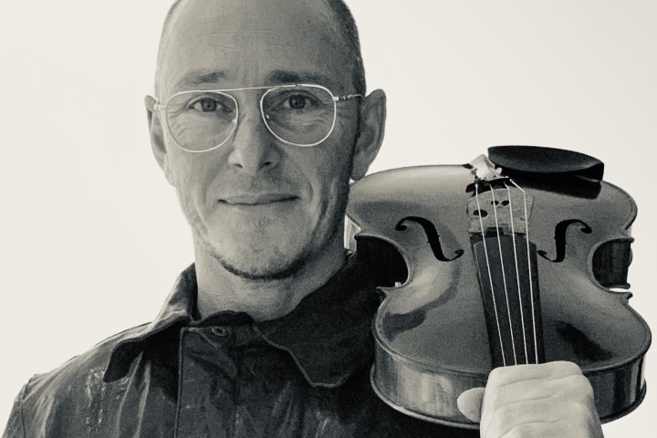 A black and white photo of Ed Ayres, holding a viola on his shoulder.