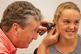 Man in red check shirt looking through otoscope into young female patients ear.
