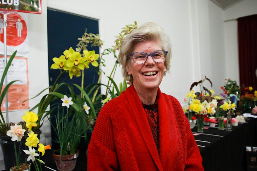 A woman smiles at the camera while standing in front of a table of daffodil flower arrangements