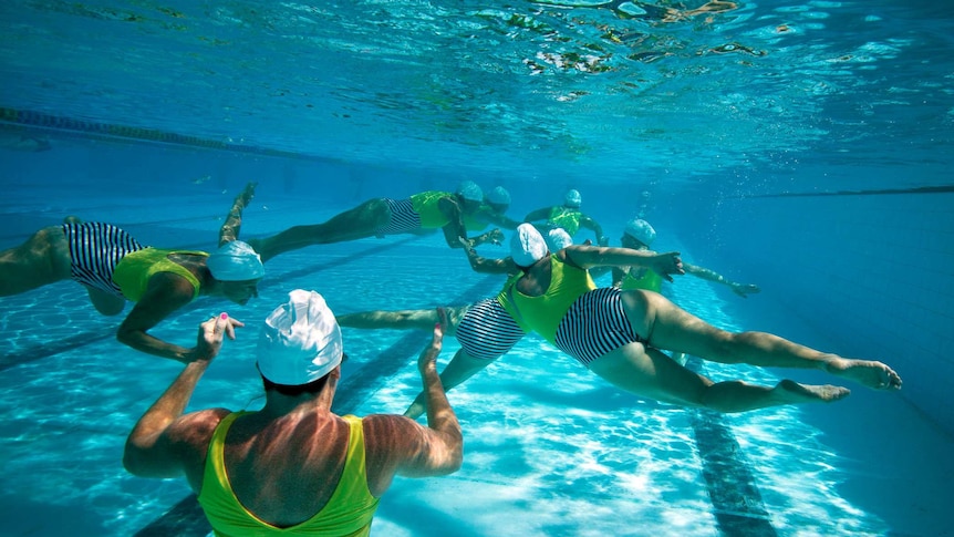 eight female synchronised swimmers in yellow bathers underwater in a pool