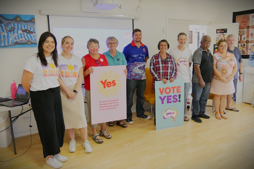10 people standing in a row, two holding up 'Yes' and 'Vote Yes' for the Voice referendum signs