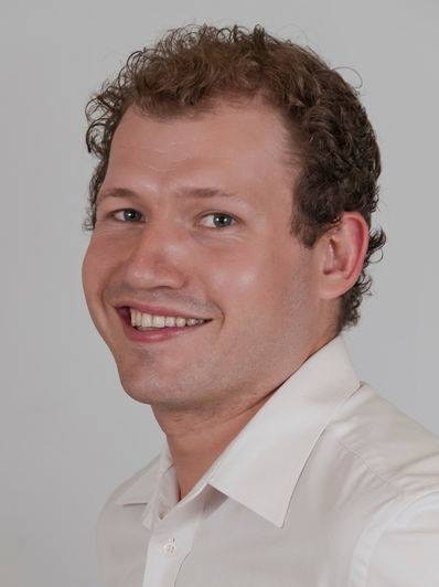 A man with dark brown hair and a white collared shirt smiling