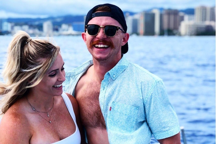 A young woman and man with their arms around each other near water.