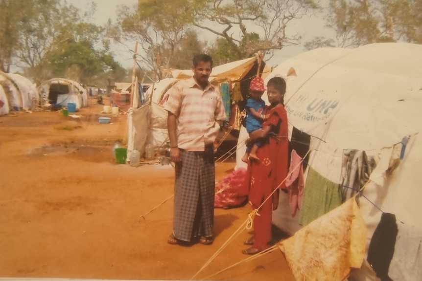 Two parents and a young child standing next to a ragged tent