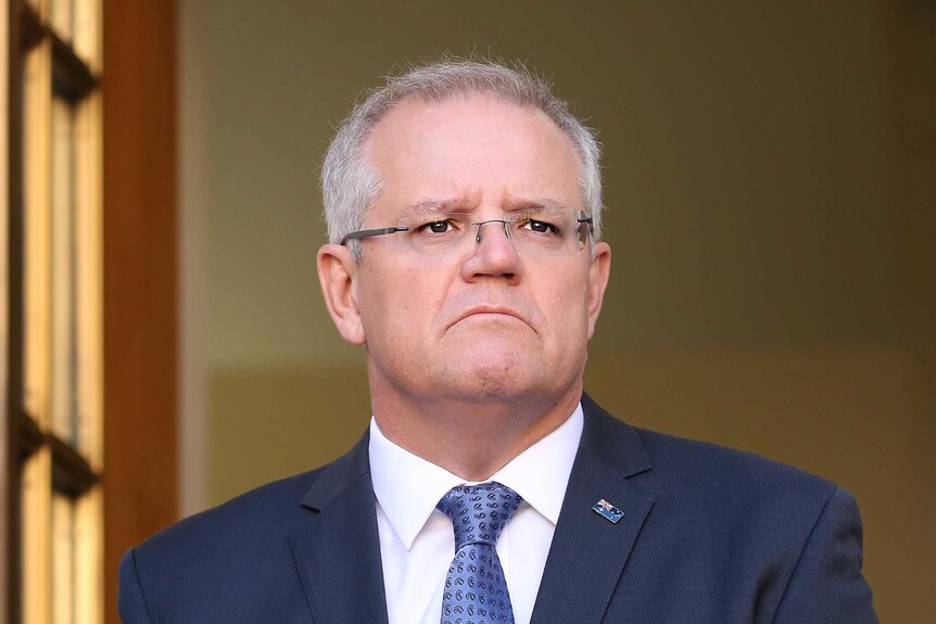 Scott Morrison frowns while standing in front of a doorway with an Australian flag beside it