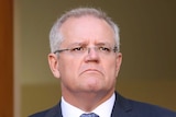 Scott Morrison frowns while standing in front of a doorway with an Australian flag beside it