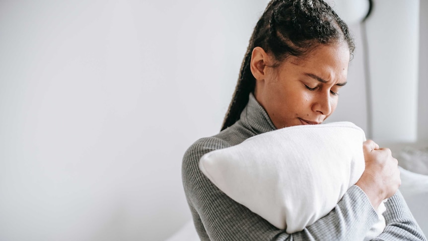 Women in grey jumper hugs a white pillow