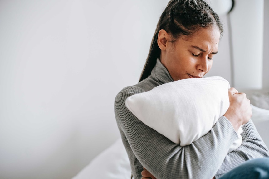 Women in grey jumper hugs a white pillow