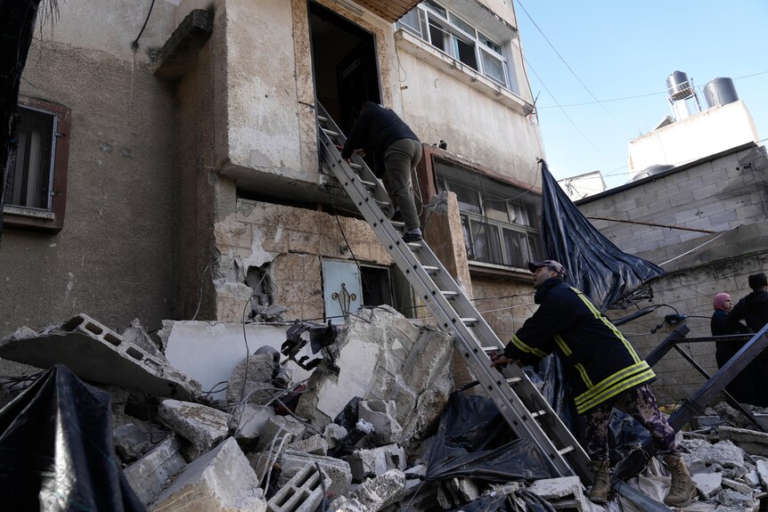 a pile of rubble next to a building, where people have used a ladder to reach into a hole in the wall