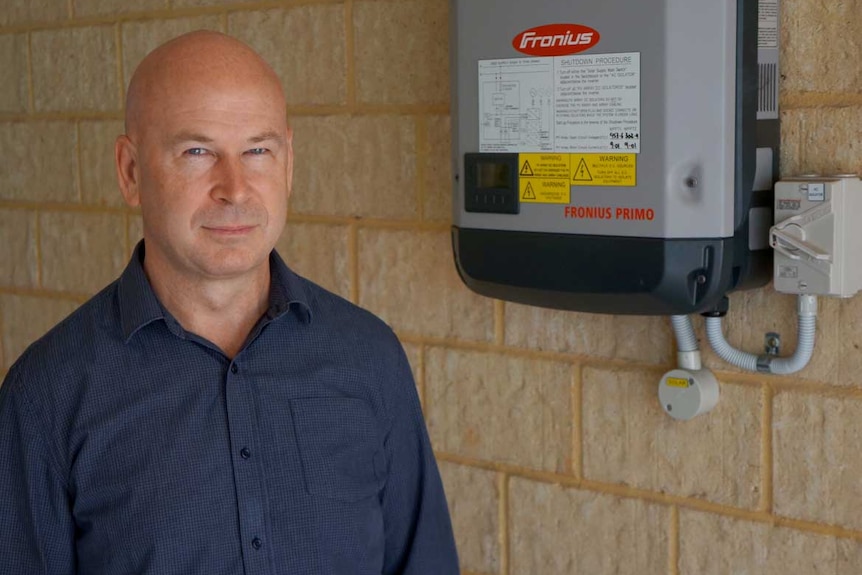 David Walker stands near a solar box on a brick wall.