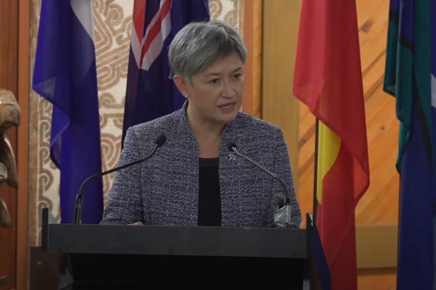 Foreign Minister Penny Wong speaking in the Pacific at a podium in front of flags.