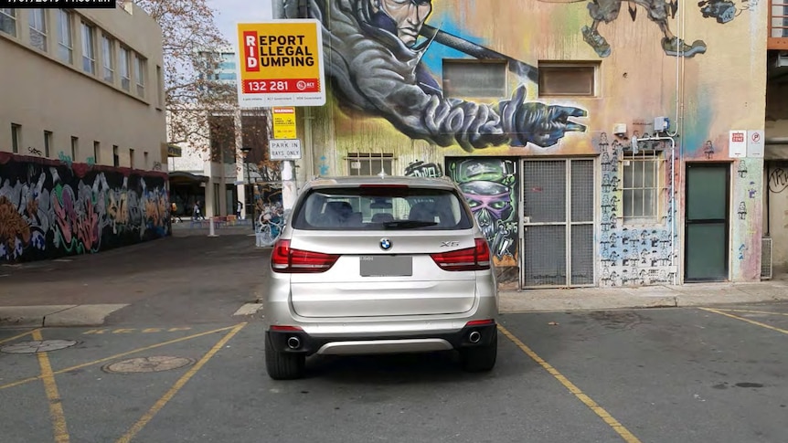 A silver BMW parked near a graffitied wall.