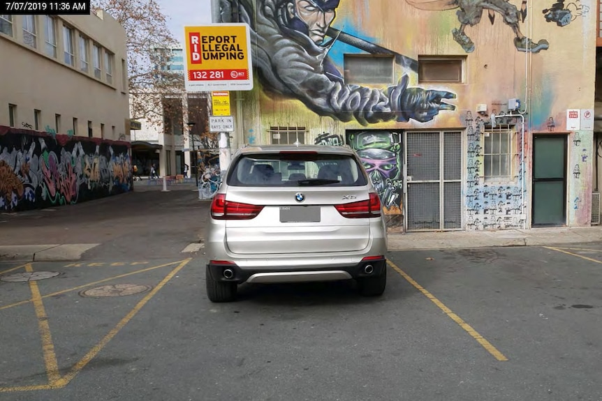 A silver BMW parked near a graffitied wall.