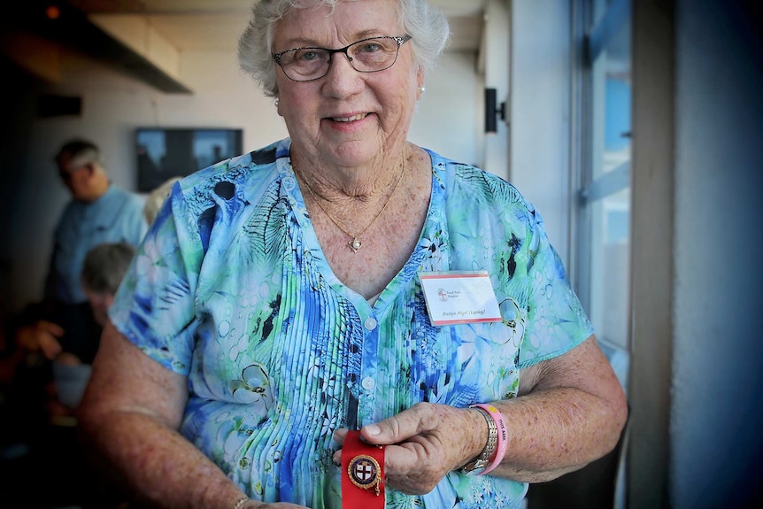 An older woman poses for a photo smiling and holding a nurses badge.