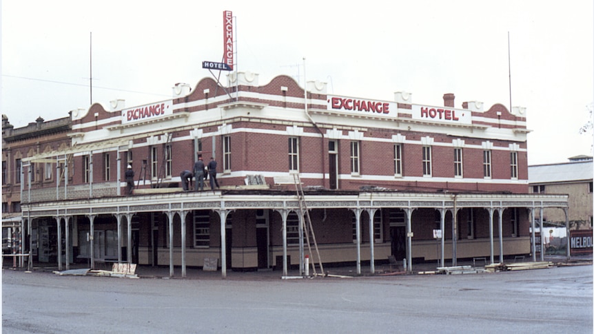 An old photo of workers removing pieces of a second-story balcony 