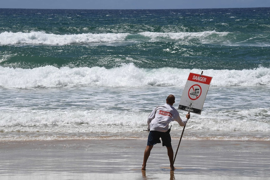A lifeguard places a danger sign on a beach on the Gold Coast.
