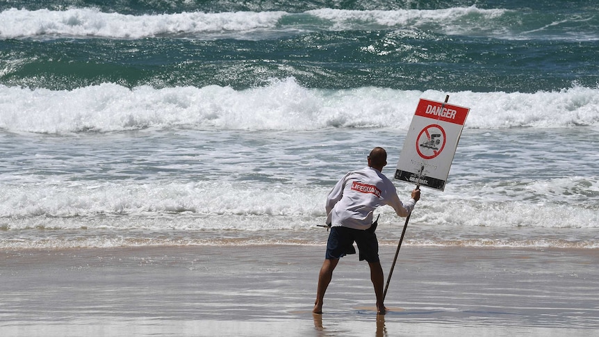 A lifeguard places a danger sign on a beach on the Gold Coast.