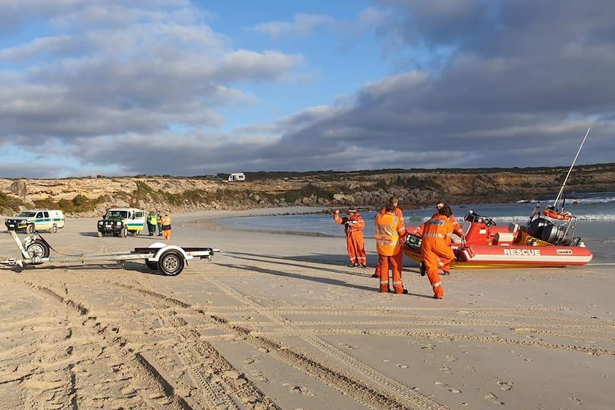State Emergency Service personnel standing on a beach beside a red rescue boat and vehicles