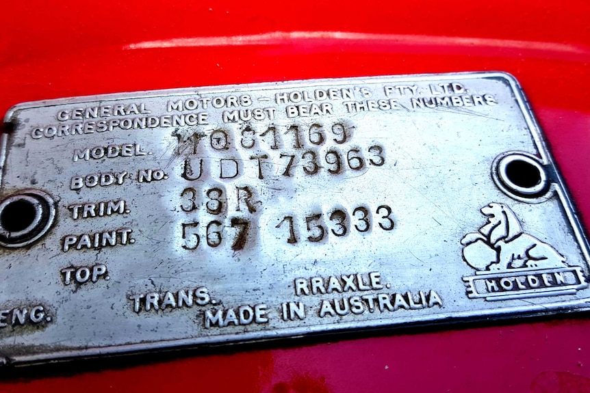 A Holden engine plate with words and numbers on a red car.