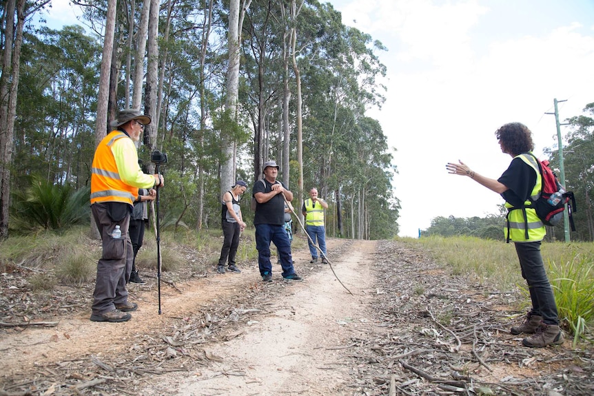 A woman holding gardening gloves and a stick pauses to think on a bush track