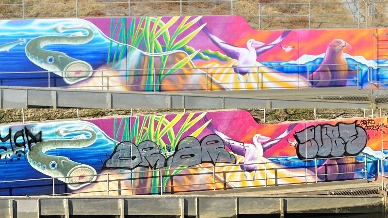 two versions of a colourful art mural on a wall by the water, image above is original, the one below is vandalised