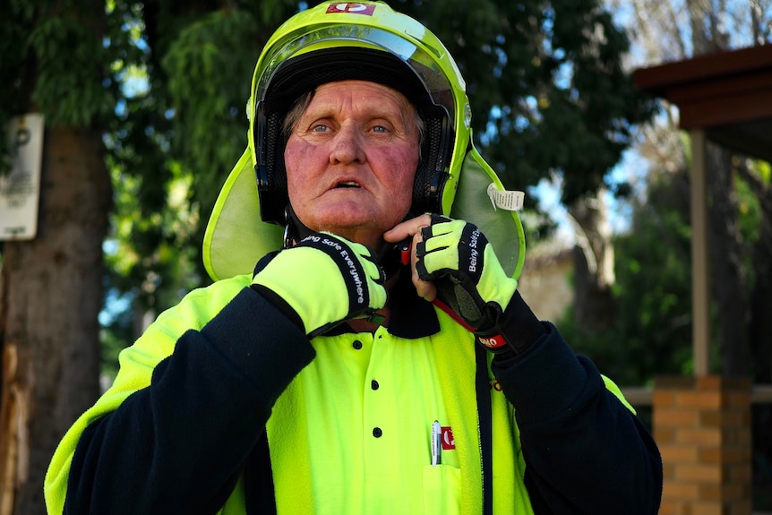 A middle aged postman dressed in fluro clothing does the buckle up on his helmet